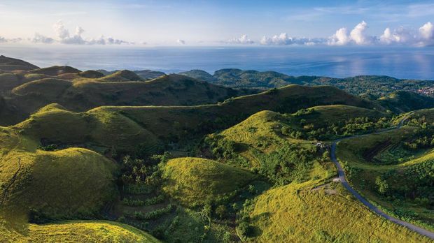 Aerial drone panoramic view at sunrise of the lush hilltops and valleys with scenic sea views and located on the island of Nusa Penida in Bali in Indonesia.