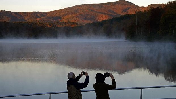 A couple takes photos as the sun rises at Price Lake along the Blue Ridge Parkway near Blowing Rock, N.C., Tuesday, Oct. 19, 2021. (AP Photo/Gerry Broome)