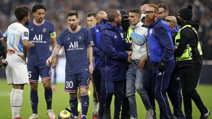 A man is apprehended by security after running onto the pitch toward PSGs Lionel Messi the pitch during the French League One soccer match between Marseille and Paris Saint-Germain in Marseille, France, Sunday, Oct. 24, 2021. (AP Photo/Daniel Cole)