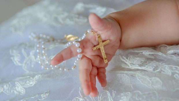 Child's hand with a crucifix on a white cloth.