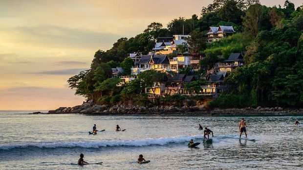 Photo taken on Oct. 25, 2021 shows people surfing on the beach in Thailand's Phuket Island, while tourists enjoy the activity. 