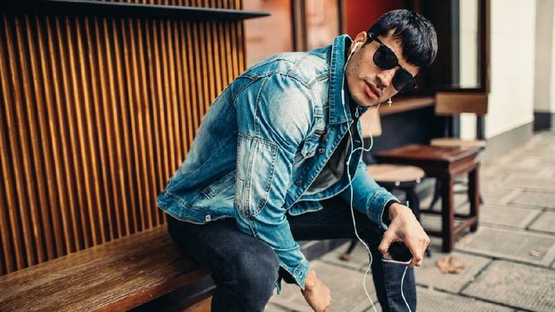 Young, handsome man in denim jacket sitting on a bench and listening to music on mobile phone