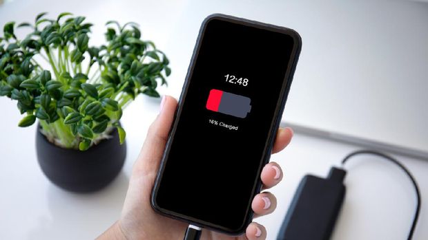 female hand holding phone with red discharged battery on screen connected to powerbank