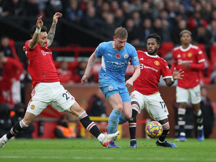 MANCHESTER, ENGLAND - NOVEMBER 06:  Kevin De Bruyne of Manchester City runs with the ball from Alex Telles and Fred of Manchester United during the Premier League match between Manchester United and Manchester City at Old Trafford on November 06, 2021 in Manchester, England. (Photo by Clive Brunskill/Getty Images)