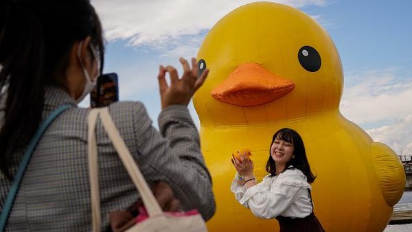 Seorang warga berfoto sembari membawa bebek karet kecil di depan sebuah bebek karet berukuran raksasa di kawasan Osaka, Jepang, Minggu (14/11/2021) waktu setempat. Seorang warga berfoto sembari membawa bebek karet kecil di depan sebuah bebek karet berukuran raksasa di kawasan Osaka, Jepang, Minggu (14/11/2021) waktu setempat.