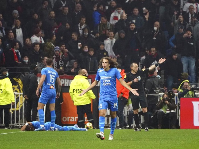 Marseille's Matteo Guendouzi gestures as his teammate Dimitri Payet lays on the field after being injured by an object thrown by a Lyon's supporter during the French League One soccer match between Lyon and Marseille, in Decines, near Lyon, central France, Sunday, Nov. 21, 2021. (AP Photo/Laurent Cipriani)