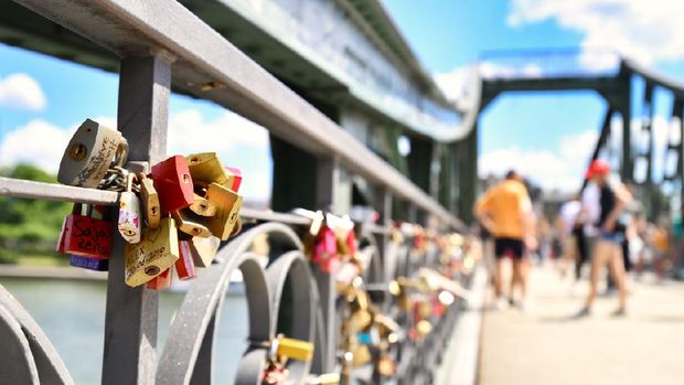 Frankfurt am Main, Germany - June 2020: Close up of love padlocks at bridge called 'Eiserner Steg' with blurry tourists in background on sunny day