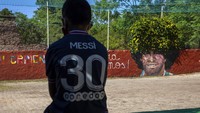 Seorang anak laki-laki mengenakan jersey PSG Leonel Messi beristirahat di dekat mural mendiang bintang sepak bola Diego Maradona di Lugar del Sol, sebuah organisasi amal yang membantu anak-anak berisiko, di Buenos Aires, Argentina. (AP/Rodrigo Abd)