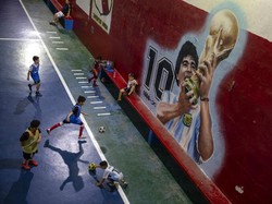 Anak-anak bermain sepak bola di dekat mural yang menampilkan mendiang bintang sepak bola Diego Maradona di klub Juventud Unida di Buenos Aires, Argentina. Peringatan pertama kematian sang legenda sepak bola jatuh pada 25 November 2021. (AP/Rodrigo Abd)