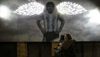 Wanita berpelukan di dekat mural mendiang bintang sepak bola Diego Maradona di Buenos Aires, Argentina. (AP/Rodrigo Abd)