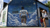 Pejalan kaki melewati mural yang menggambarkan mendiang legenda sepak bola Diego Maradona di kawasan Lomas de Marilo, Buenos Aires, Argentina. (AP/Gustavo Garello)