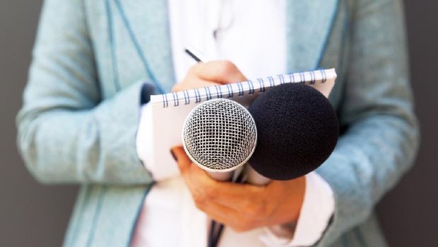 Female reporter at press conference, writing notes, holding microphone