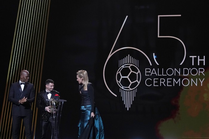 PSG player Lionel Messi , centrem=, flanked with hosts former Chelsea striker Didier Drogba, left, and French journalist Sandy Heribert, right, reacts after winning the 2021 Ballon dOr trophy during the 65th Ballon dOr ceremony at Theatre du Chatelet, in Paris, Monday, Nov. 29, 2021. Messi won the Ballon dOr for seventh time. (AP Photo/Christophe Ena)