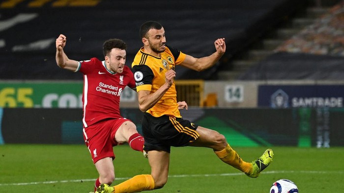 WOLVERHAMPTON, ENGLAND - MARCH 15: Diogo Jota of Liverpool scores their sides first goal whilst under pressure from Romain Saiss of Wolverhampton Wanderers during the Premier League match between Wolverhampton Wanderers and Liverpool at Molineux on March 15, 2021 in Wolverhampton, England. Sporting stadiums around the UK remain under strict restrictions due to the Coronavirus Pandemic as Government social distancing laws prohibit fans inside venues resulting in games being played behind closed doors. (Photo by Paul Ellis - Pool/Getty Images)