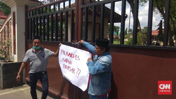 Massa pedemo yang menolak penundaan pilkades menyegel dengan gembok Rumah Dinas Bupati Pamekasan di Jalan Kabupaten. (CNN Indonesia/Nurus Solehen)