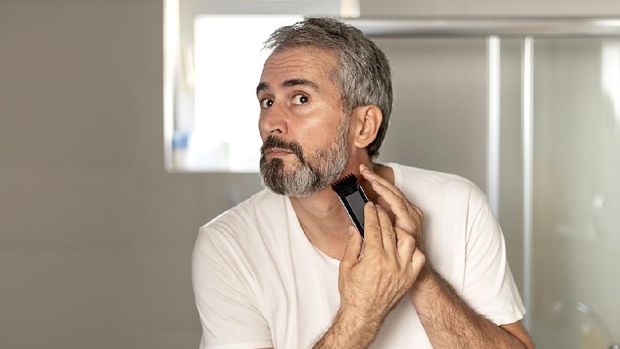 Handsome Mature Bearded Man Trimming His Beard With a Trimmer at Morning in the Bath Room. Beauty, Hygiene, Shaving, Grooming and People Concept