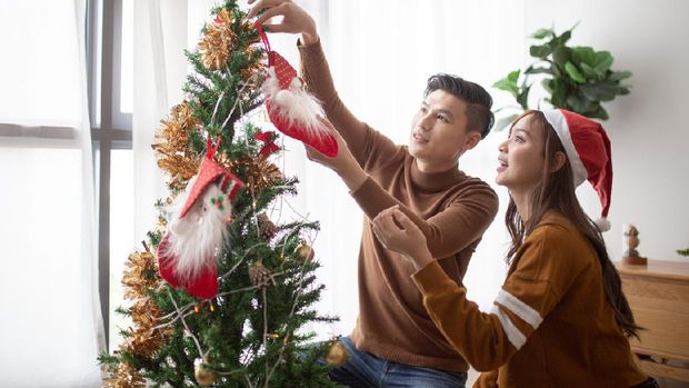 Asian Chinese couple decorating Christmas tree at home ready for Christmas celebration