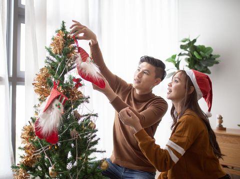 Asian Chinese couple decorating Christmas tree at home ready for Christmas celebration