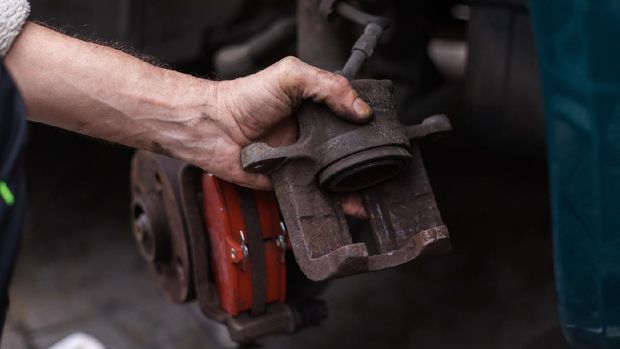 DIY - man repairing disc brake at vintage car, replacing brake pads at parking lot, hand holds caliper with brake piston