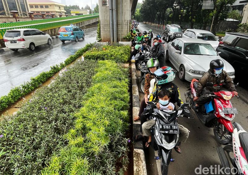 Sejumlah pengendara motor berteduh di kolong jembatan layang bus TransJakarta, Selasa (28/12/2021). Meski membuat lalu lintas macet, mereka nekat berteduh agar terhindar dari guyuran hujan.