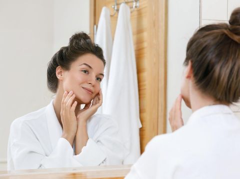 Young woman is looking into the mirror at morning