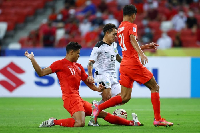 SINGAPORE, SINGAPORE - DECEMBER 14: Paulo Domingos Gali #21 of Timor-Leste shoots the ball against Irfan Fandi #17 and Safuwan Baharudin #21 of Singapore during the second half of their AFF Suzuki Cup Group A game at the National Stadium on December 14, 2021 in Singapore. (Photo by Yong Teck Lim/Getty Images)
