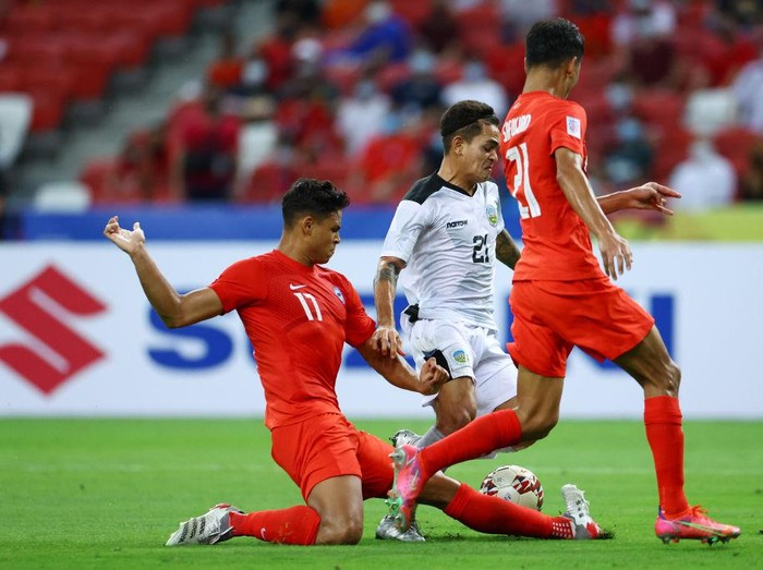 SINGAPORE, SINGAPORE - DECEMBER 14: Paulo Domingos Gali #21 of Timor-Leste shoots the ball against Irfan Fandi #17 and Safuwan Baharudin #21 of Singapore during the second half of their AFF Suzuki Cup Group A game at the National Stadium on December 14, 2021 in Singapore. (Photo by Yong Teck Lim/Getty Images)