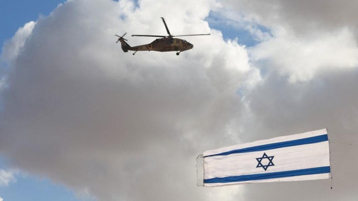 Israeli Blackhawk helicopter perform with flag during an air show as part of a graduation ceremony of Israeli pilots at the Hatzerim air force base in the southern Negev desert, near the city of Beersheva,on December 22, 2021. (Photo by Menahem KAHANA / AFP)