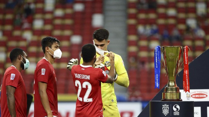 Yabes Roni Malaifani of Indonesia, third left, assists Nadeo Arga Winata of Indonesia puts on the mask during the prize presentation of the AFF Suzuki Cup 2020 final in Singapore, Saturday, Jan. 1, 2022. (AP Photo/Suhaimi Abdullah)
