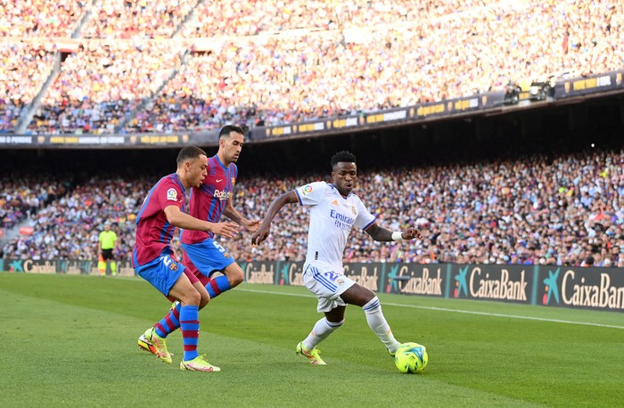 BARCELONA, SPAIN - OCTOBER 24: Vinicius Junior of Real Madrid holds off Sergino Dest and Sergio Busquets of FC Barcelona during the LaLiga Santander match between FC Barcelona and Real Madrid CF at Camp Nou on October 24, 2021 in Barcelona, Spain. (Photo by David Ramos/Getty Images)
