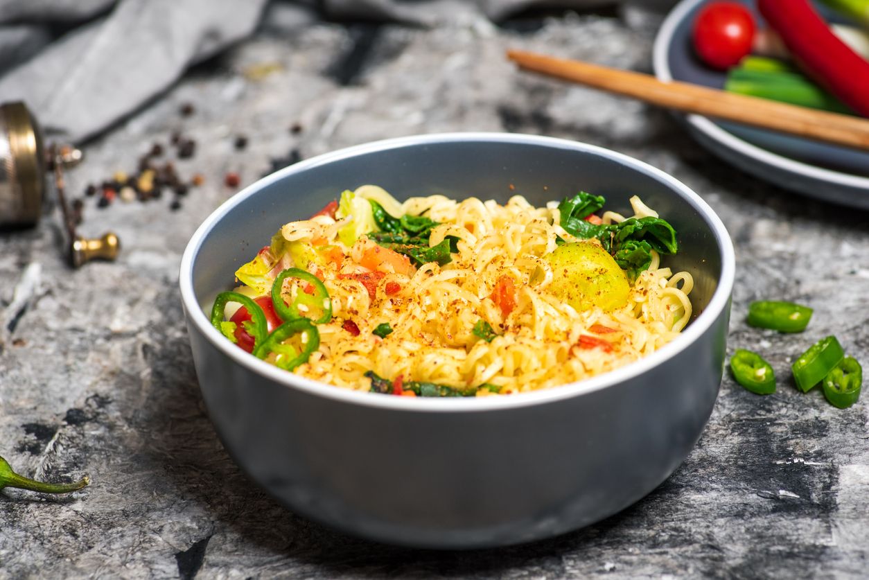 Bowl of cooked instant noodles with spices food ingredients on a grey wooden table tabletop view