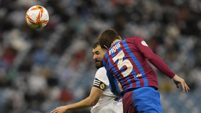 Real Madrids Karim Benzema heads the ball in front of Barcelonas Gerard Pique during the Spanish Super Cup semi final soccer match between Barcelona and Real Madrid at King Fahd stadium in Riyadh, Saudi Arabia, Thursday, Jan. 13, 2022. (AP Photo/Hassan Ammar)