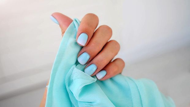 Female hands with a beautiful gentle manicure. Summer trend, blue gradient on the nails with gel polish, shellac. Short nails