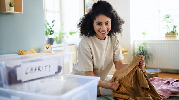 Happy young woman sorting wardrobe indoors at home, charity donation concept.