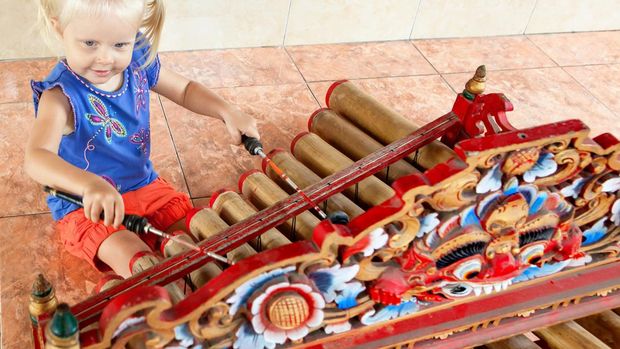 Little funny child play music on traditional indonesian musical instrument - bamboo xylophone Rindik or Tingklik. Arts, culture of Bali island and Indonesia.