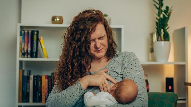 Newly mother breastfeeding her newborn baby boy while in pain
