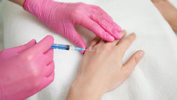 Close-up of a female professional injecting enhancement pills into the arm of a female colleague