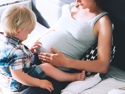 Pregnant mother and son are talking and spending time together in bed at home. Little child boy looking at her mother pregnant tummy. Pregnancy, family, parenthood, preparation and expectation concepts.