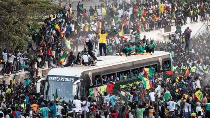 Supporters cheer as Aliou Cisse the Senegalese Football teams coach raises the trophy in Dakar on February 7, 2022,  after winning, for the first time, the Africa Cup of Nations. - Senegals President Macky Sall declared February 7, 2022, a public holiday to celebrate the national football teams first ever African Cup of Nations crown following their victory against Egypt. (Photo by JOHN WESSELS / AFP)