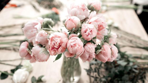 Pink peonies in vase on wooden floor and bokeh background - retro styled photo.