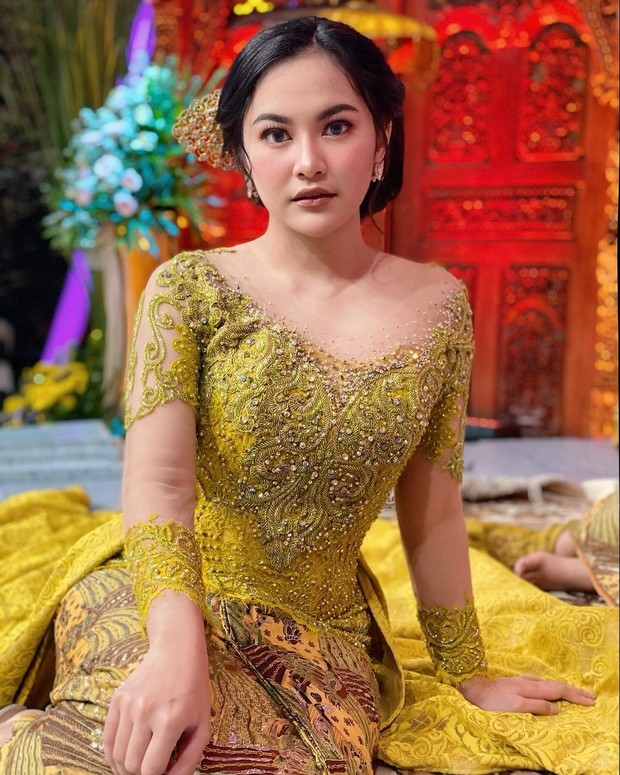 Selalu tampil cantik dengan mengenakan kebaya, Mahalini kali ini mengenakan kebaya berwarna emas dengan model sabrina memberi kesan dewasa nan anggun.