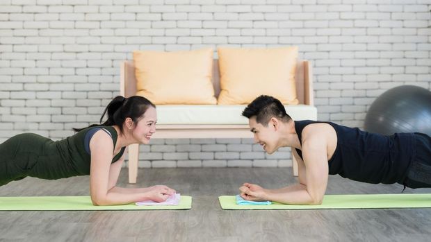 Happy asian couple doing plank exercise together in living room at home. Sporty woman and man smile and make exercise on yoga mat indoors daily routine while social distancing. Home fitness concept.