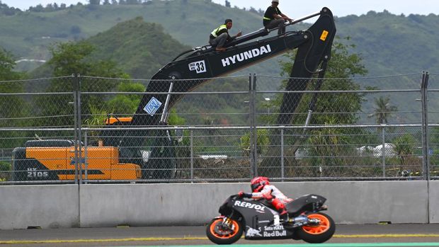 Pekerja menaiki ekskavator untuk menonton jalannya tes pramusim MotoGP 2022 dengan latar depan pembalap Repsol Honda Team MotoGP Marc Marquez di Pertamina Mandalika International Street Circuit, Lombok Tengah, NTB, Jumat (11/2/2022). Sesi tes pramusim di sirkuit Mandalika tersebut akan berlangsung hingga Minggu (13/2/2022). ANTARA FOTO/Andika Wahyu/rwa.