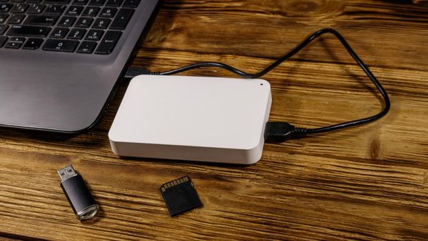 ilustrasi hard disk laptop External backup disk hard drive connected to laptop. Man with notebook making safety personal data copy.