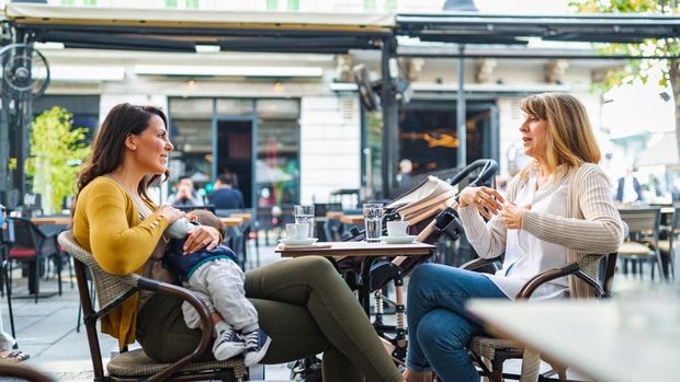 Young mother breastfeeding her baby boy in public while sitting in a cafe with her mother