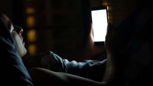 Gadis di tempat tidur sebelum tertidur melihat smartphone.  Periksa berita dan jejaring sosial sebelum tidur.  Gadget pintar.