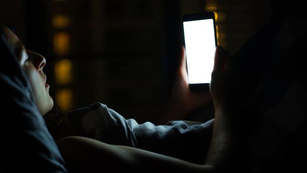 Girl on the bed before falling asleep looks at a smartphone. Check news and social networks before going to bed. Smart gadget.