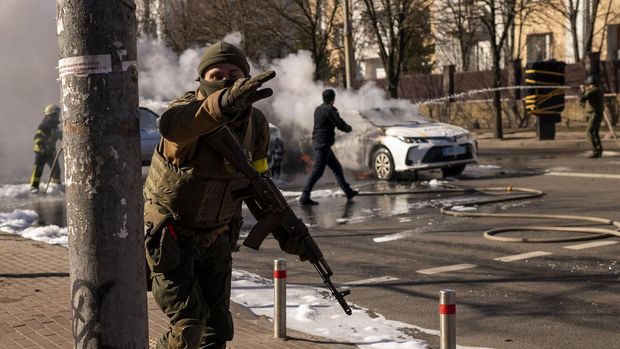 Ukrainian soldiers take positions outside a military facility as two cars burn, in a street in Kyiv, Ukraine, Saturday, Feb. 26, 2022. Russian troops stormed toward Ukraine's capital Saturday, and street fighting broke out as city officials urged residents to take shelter. (AP Photo/Emilio Morenatti)