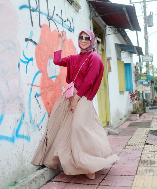 Marini Zumarnis tampil dengan mengenakan hijab dan outfit sweater berwarna pink fanta dipadukan rok plisket potongan megar.