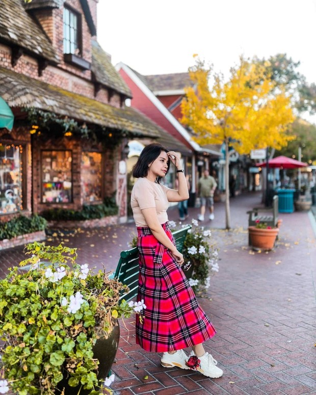 Rossa tampil seperti K-Pop idol dengan menggunak outfit simple kaos warna coklat dan rok motif kotak disempurnakan dengan sneakers berwarna putih.